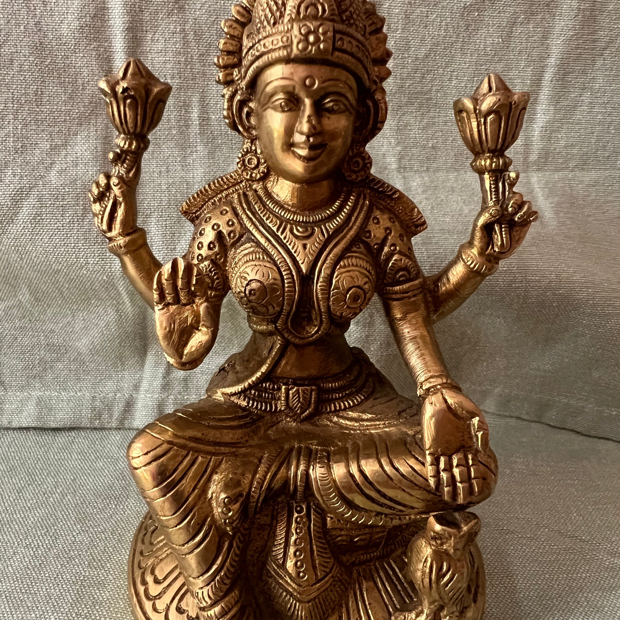 This brass Lakshmi statue from Saanskrityam Handicraft Store features the Goddess MahaLakshmi seated with four arms. She holds lotus flowers in two hands while displaying symbolic gestures with the others. Adorned with intricate jewelry and a serene expression, she embodies wealth and prosperity, making it an ideal choice for festive and auspicious gifts.