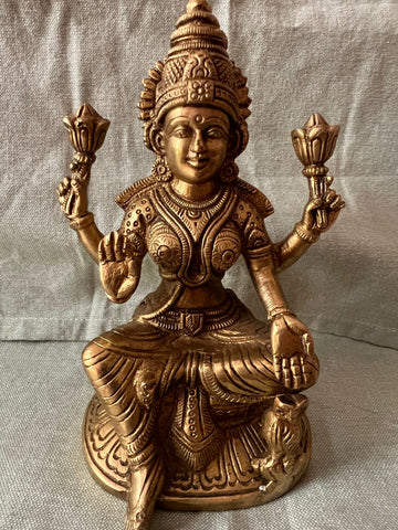 This brass Lakshmi statue from Saanskrityam Handicraft Store features the Goddess MahaLakshmi seated with four arms. She holds lotus flowers in two hands while displaying symbolic gestures with the others. Adorned with intricate jewelry and a serene expression, she embodies wealth and prosperity, making it an ideal choice for festive and auspicious gifts.