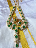 A piece from Saanskrityam Handicraft Store's collection, the Jewellery/Indian cosmetic jewellery with stones and metal, featuring a gold chain entwined with vibrant green gemstones reminiscent of traditional Indian style, is beautifully draped over a textured wooden surface. The muted dark background enhances the contrast and richness of this exquisite piece.