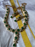 A piece from Saanskrityam Handicraft Store's collection, the Jewellery/Indian cosmetic jewellery with stones and metal, featuring a gold chain entwined with vibrant green gemstones reminiscent of traditional Indian style, is beautifully draped over a textured wooden surface. The muted dark background enhances the contrast and richness of this exquisite piece.