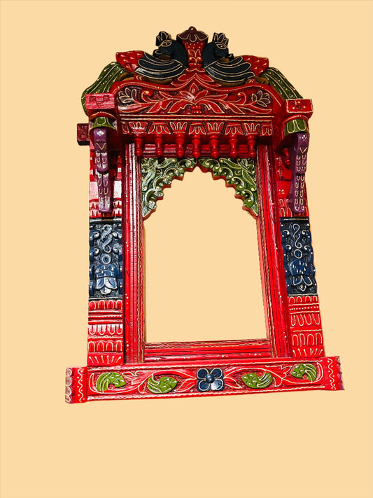 Introducing the Jaipur Peacock Jharokha, an ornate window frame by Saanskrityam Handicraft Store. This decorative piece is crafted from wood and painted with intricate red, green, and gold designs inspired by traditional Rajasthani art. The top of the jharokha features abstract animal figures accompanied by floral and geometric motifs. It serves as a striking home decor statement piece against a plain brown background.