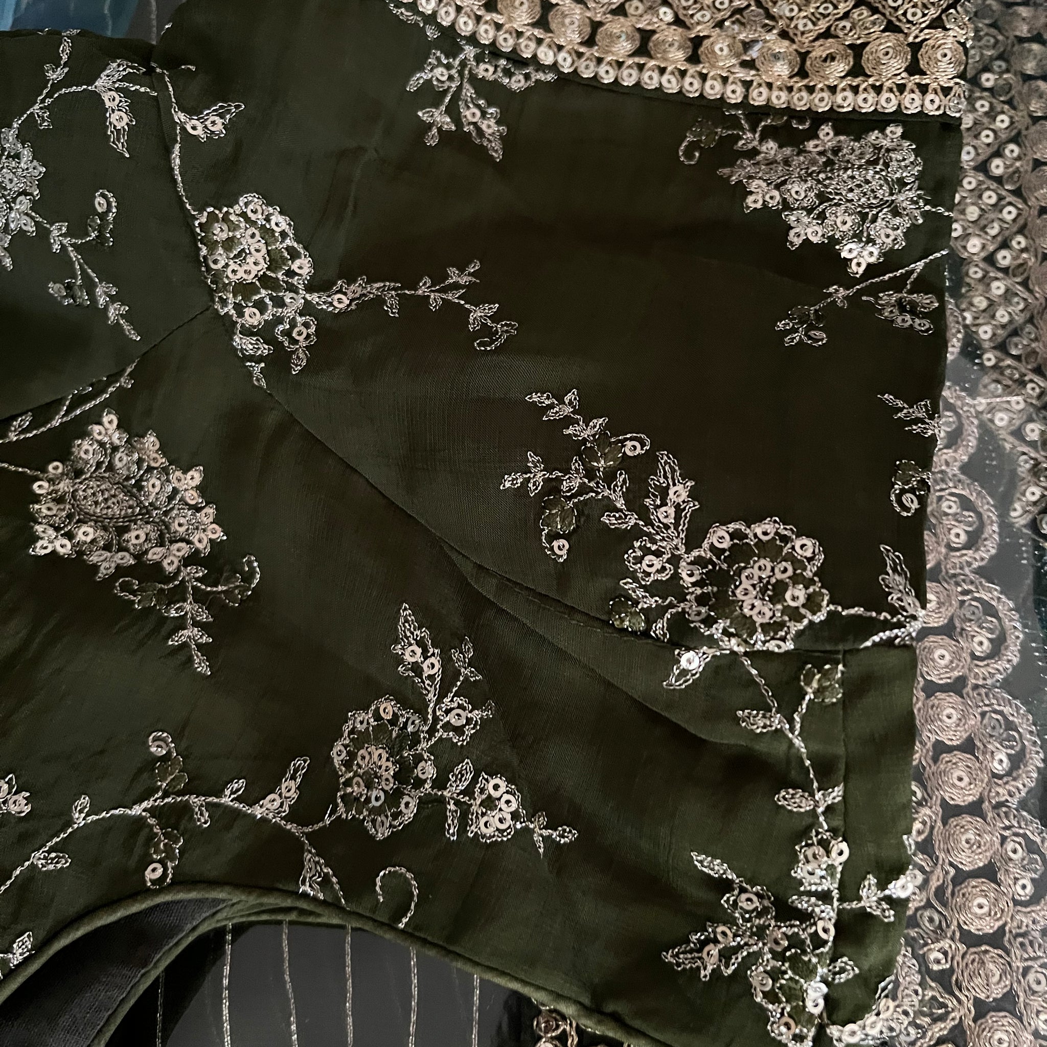 A detailed, close-up view of intricate silver Zardosi embroidery on dark green fabric, featuring floral and geometric patterns. This exquisite embroidery enhances a Party wear finished Indian saree from Saanskrityam Handicraft Store, complete with an embroidered and embellished stitched blouse in size large.