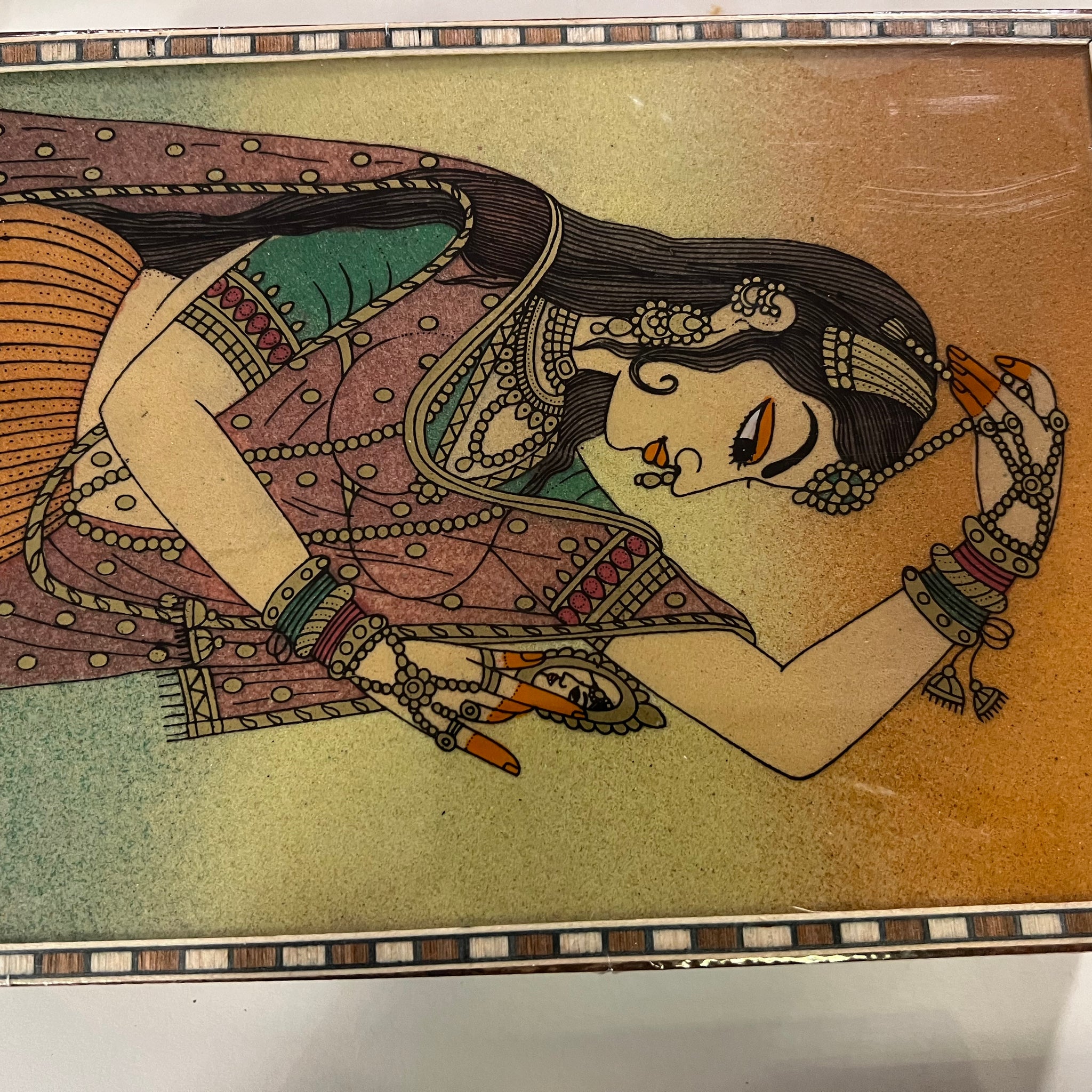 The "Women's gifts Saanskrityam" by Saanskrityam Handicraft Store features a vibrant painting of a woman in traditional attire, embellished with bangles and jewelry, lying on her side like a Meenakari jewel box. The woman rests her head on her hand amidst intricate patterns and vivid colors that evoke the essence of Madhubani art.