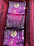 Three packages of the Indian Music Collection incense sticks from Saanskrityam Handicraft Store are arranged on a red fabric. The purple boxes with gold text, featuring an OM symbol and various logos, evoke rich fragrances akin to the soothing notes of Carnatic music.